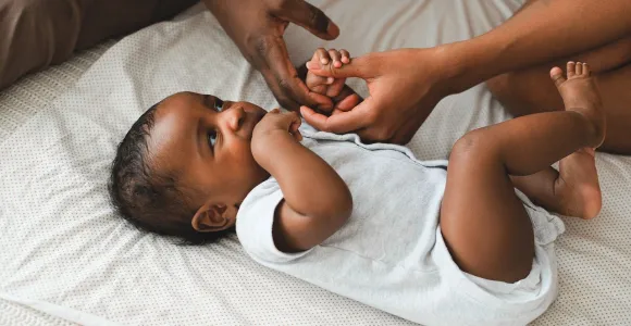 Zwarte baby ligt op de rug en wordt bij handje genomen door ouders