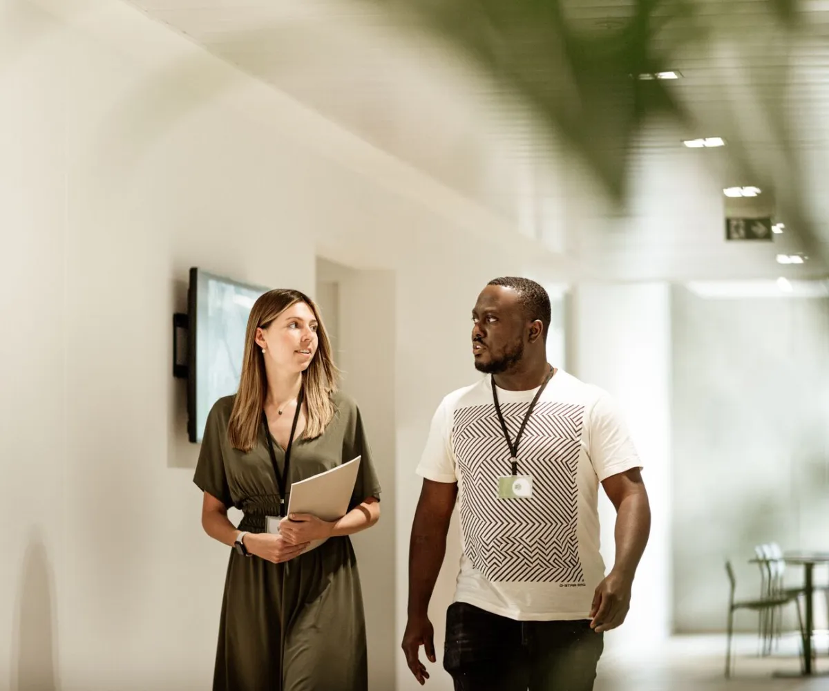 Werken bij CM; twee collega's lopen samen door de gang.