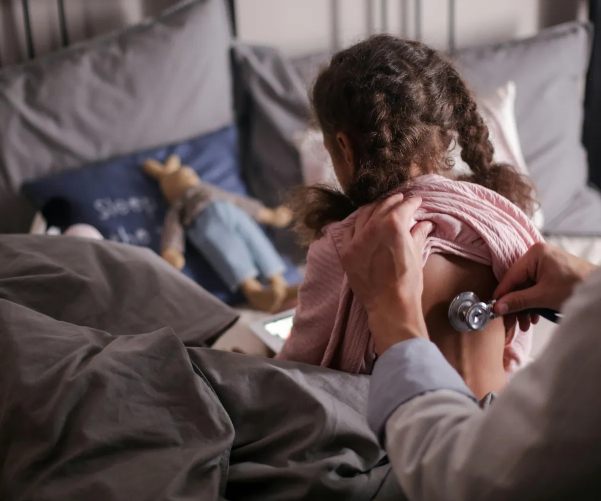meisje zit in bed en dokter houdt stethoscoop tegen haar rug